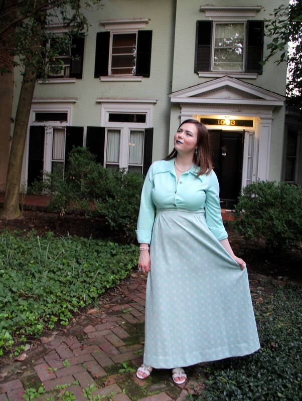 Executive editor Gretchen Gales. White, femme person with brown hair and a long green dress standing in front of a white house.