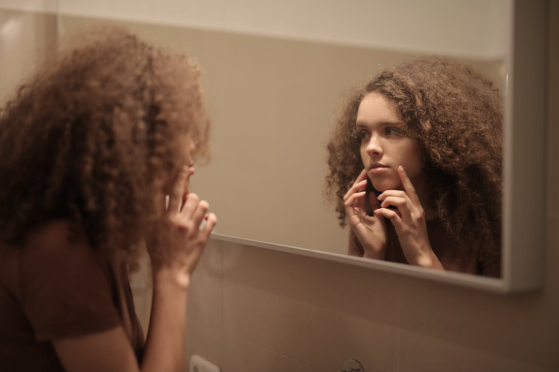 Young woman with curly hair touching her face while looking in the mirror. 