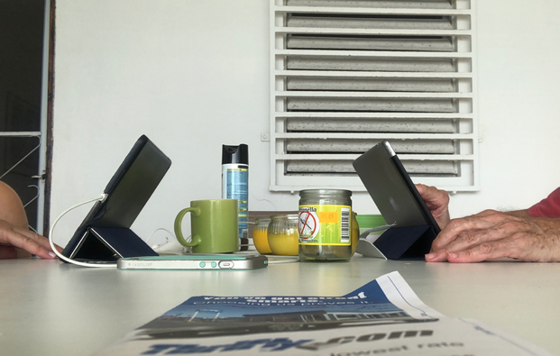 Two light-skinned people with their iPads at a table with candles, bug spray, and a mug